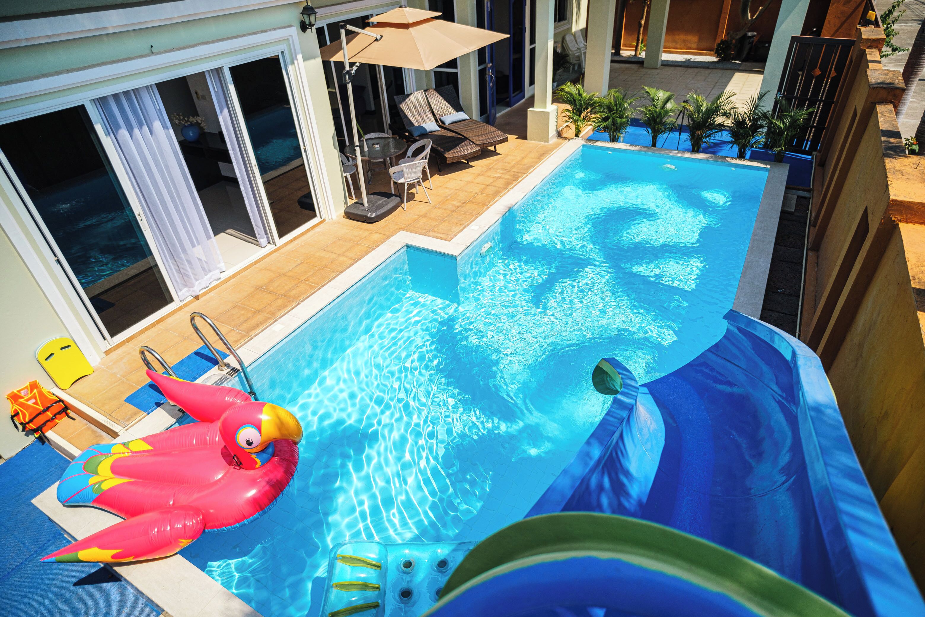 Une piscine avec un toboggan, des chaises longues et un flamant rose gonflable.