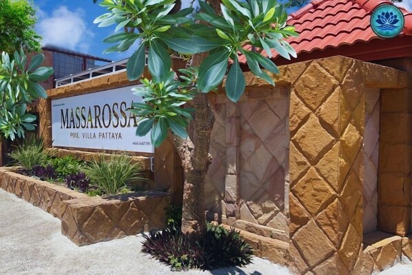 Letrero que dice 'MASSAROSSA POOL VILLA PATTAYA', con un muro de piedra y un techo rojo.