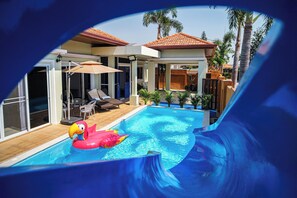 Una piscina con tobogán, sillas de descanso y un patio con sombrillas.