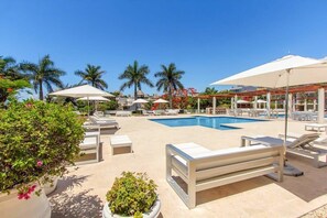A pool area with lounge chairs and umbrellas, surrounded by palm trees and potted plants.