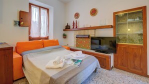 Una habitación de hotel con una cama, televisión, armario de madera y ventana con cortinas.