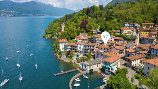 Un pueblo costero con un puerto deportivo, casas de techo rojo y una montaña al fondo.