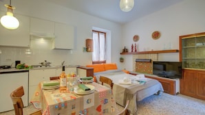 Una cocina compacta con armarios blancos, un comedor con mesa lista para dos personas y un televisor en una esquina.