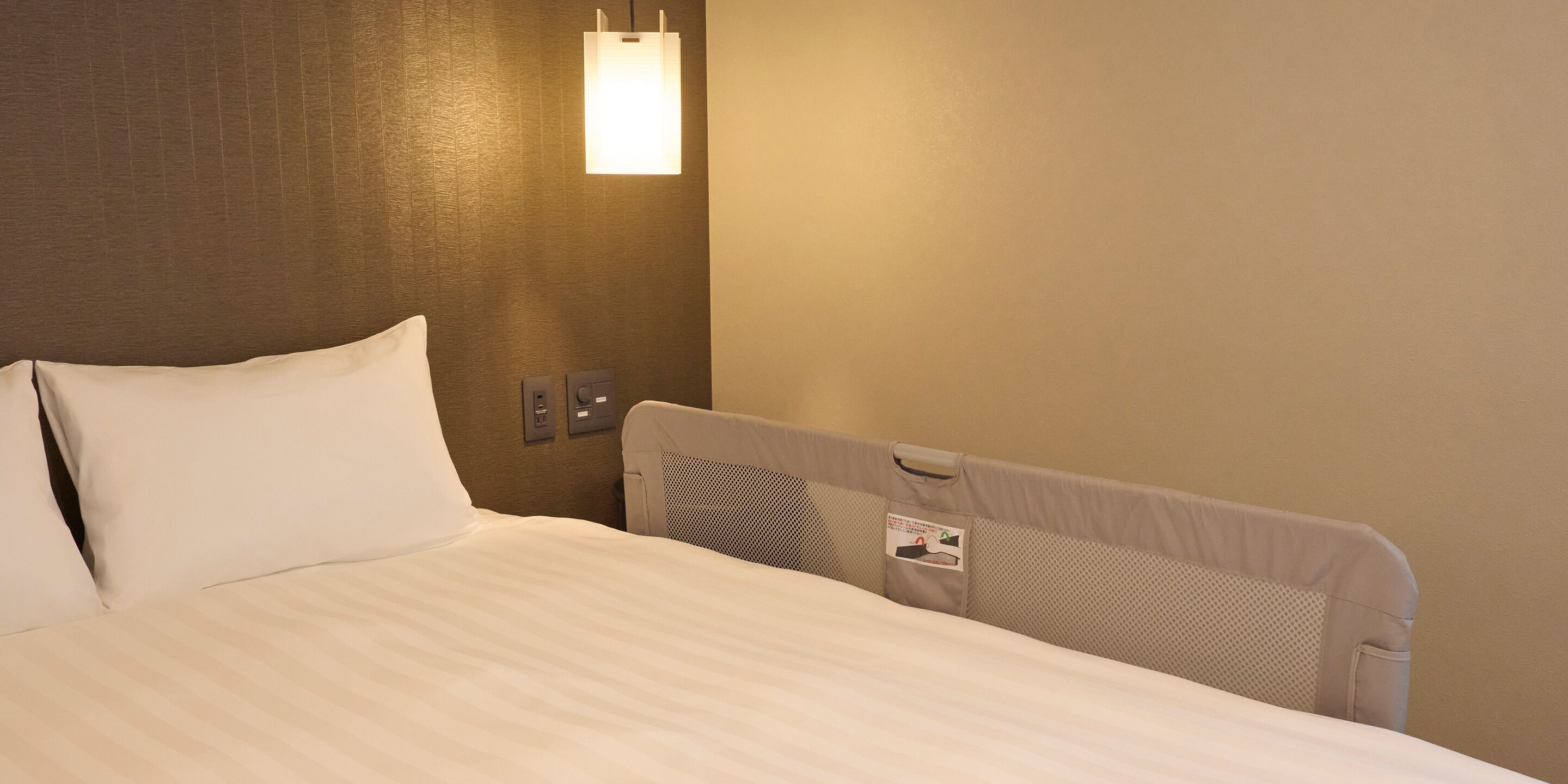 Una habitación de hotel con una cama bien hecha, una lámpara fijada en la pared y un panel de control en la pared.