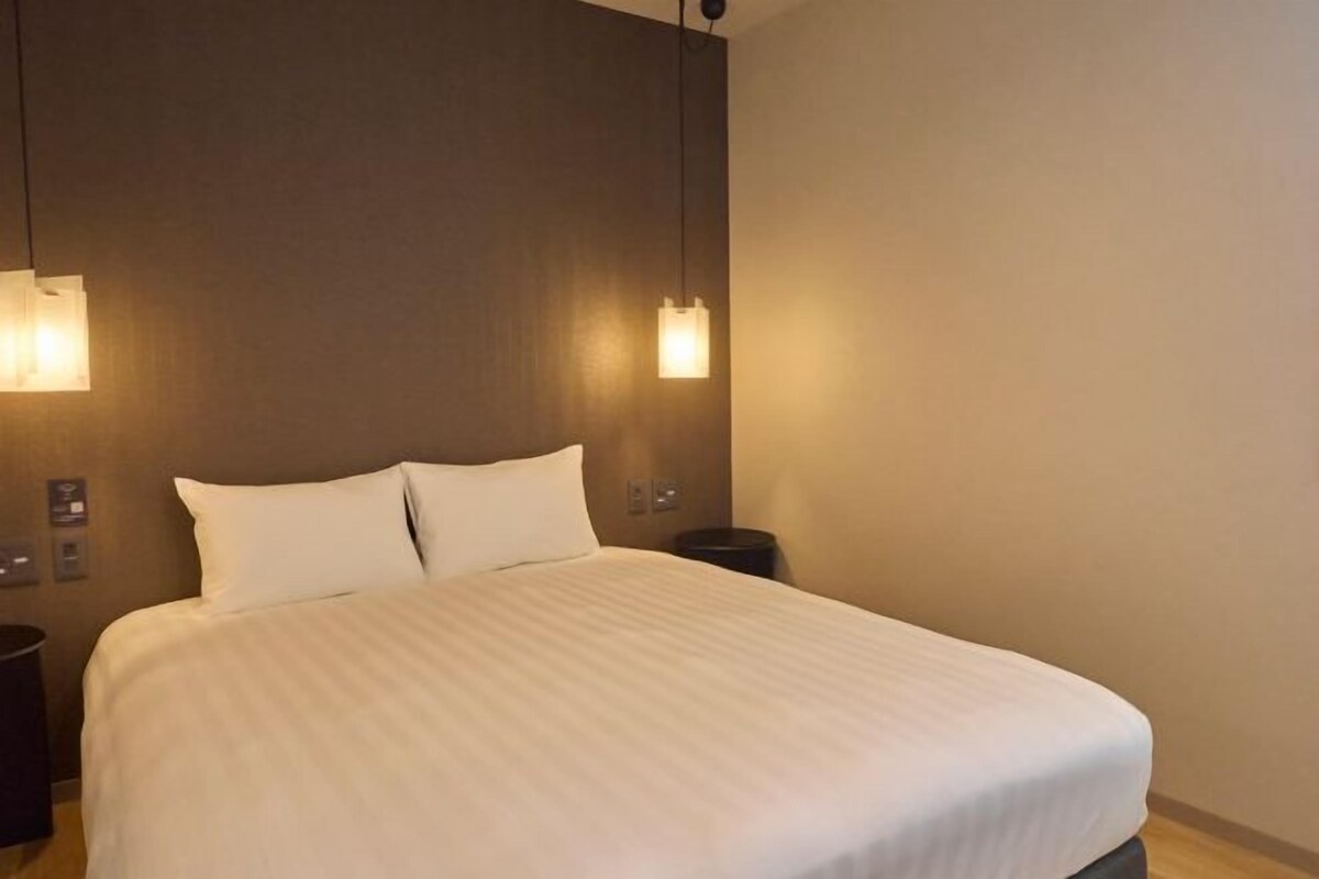 A hotel room with a large bed, two bedside lamps, a nightstand, and a wall-mounted light fixture.