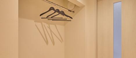 A closet with three black hangers on a rod.