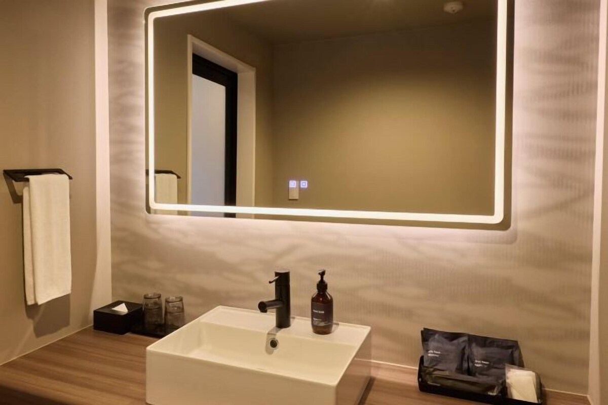 Une salle de bain avec un lavabo blanc, un miroir dont les bords sont éclairés, un porte-serviettes et une petite poubelle.