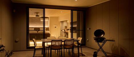 A modern dining area with a table and chairs, a grill, and a sliding glass door leading to a bedroom.