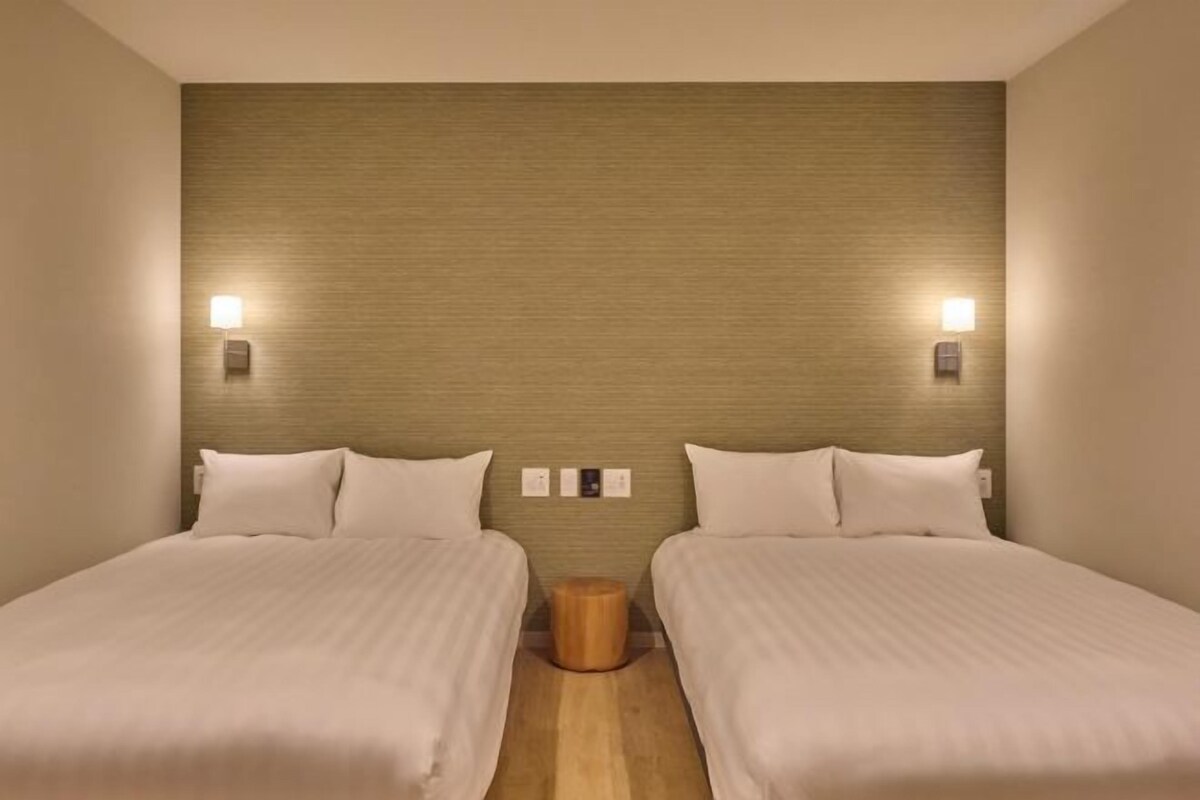 Une chambre double avec deux lits, une table de chevet en bois et des lampes fixées au mur.