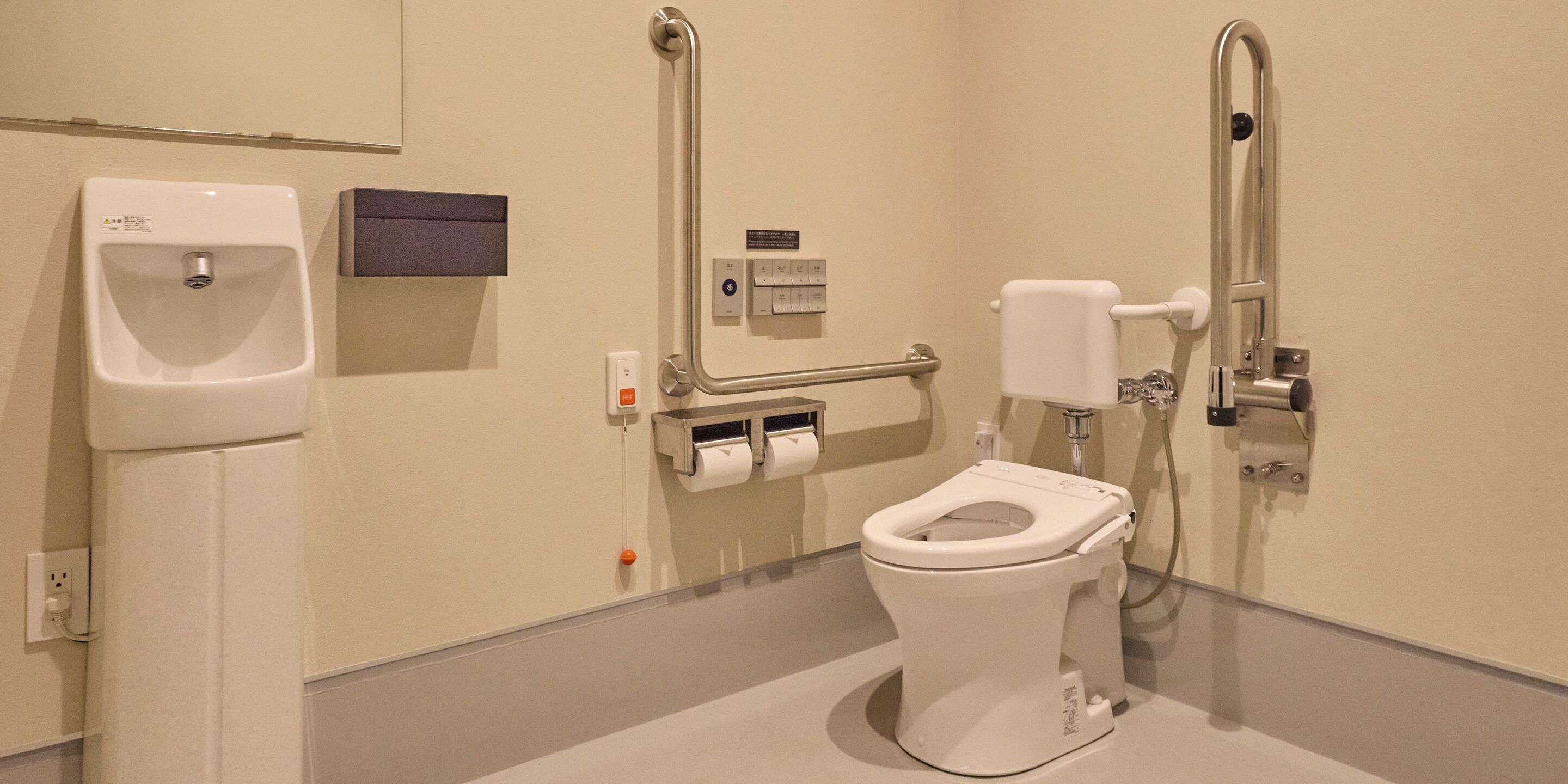 A modern bathroom with a toilet, urinal, and hand sanitizer dispenser.