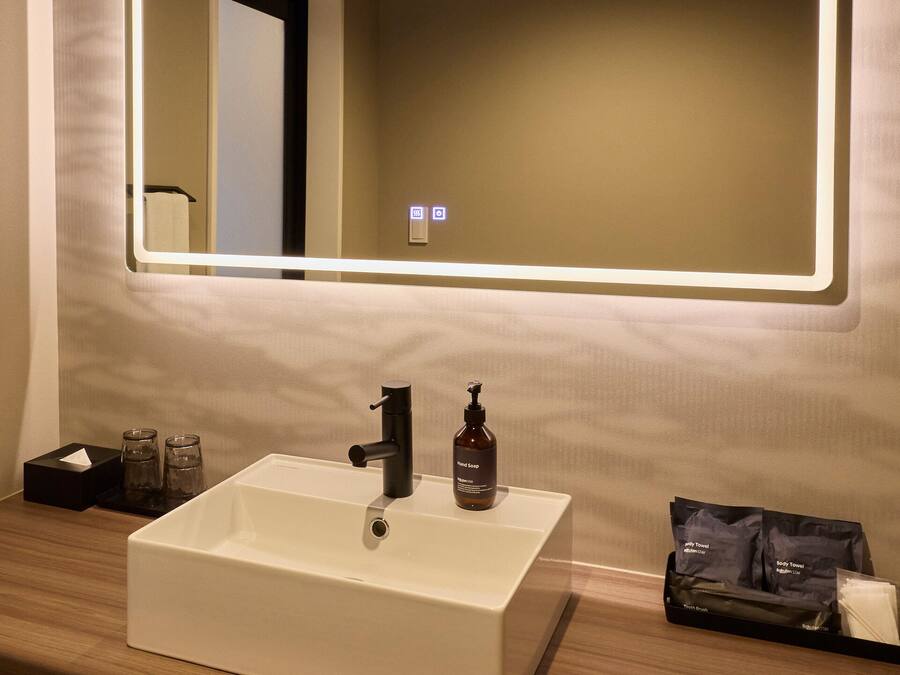 A modern bathroom with a white sink, a mirror, and a hand soap dispenser.