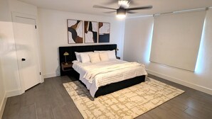 A bedroom with a bed, a nightstand, a ceiling fan, a patterned rug, and abstract wall art. - Time to Grill with Gas BBQ, Smoker, with Big Yard. Large office and new appliances (Round Rock)