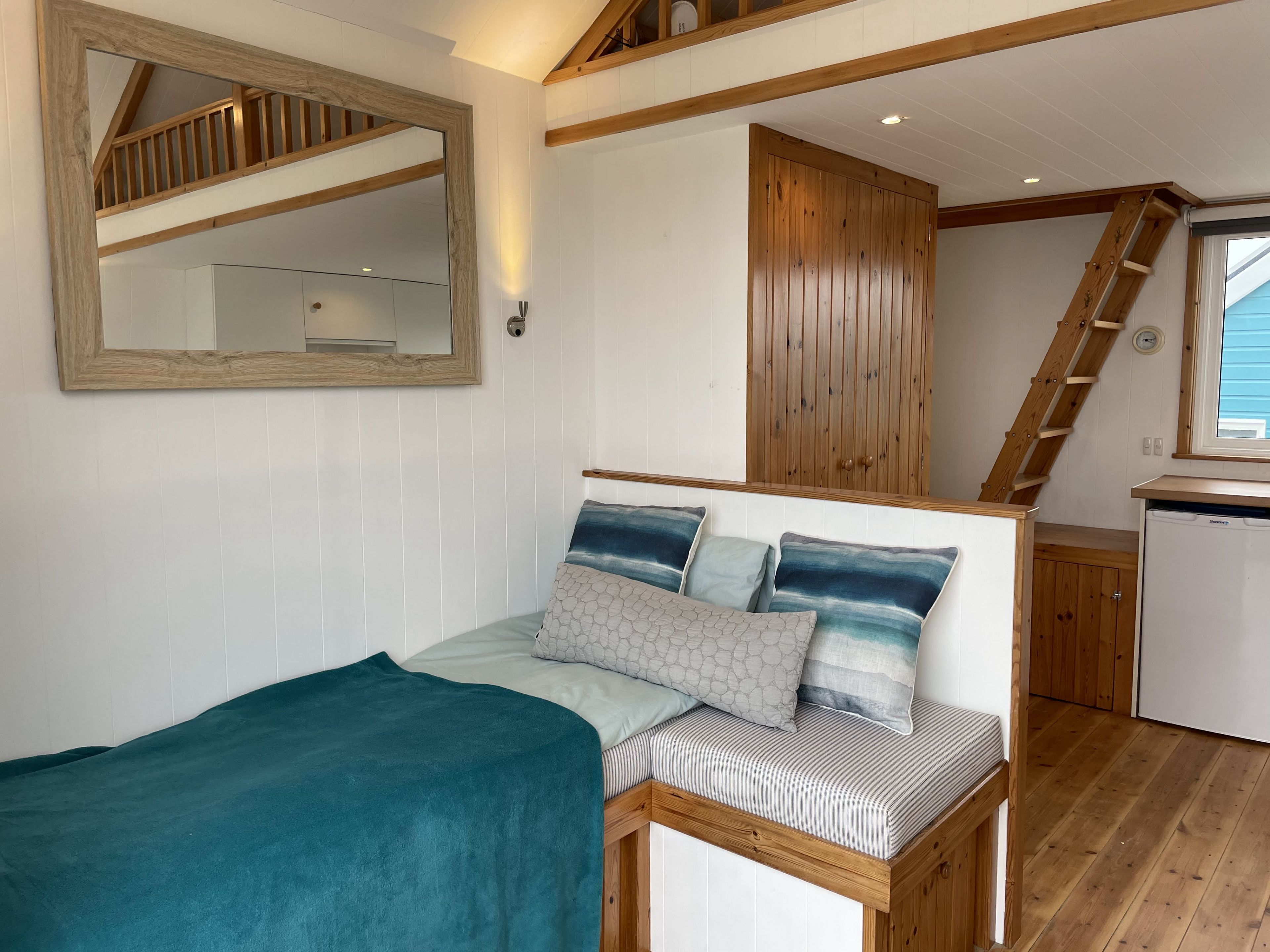 A bedroom with a bed, a wooden headboard, a mirror, a wardrobe, and a staircase leading to an upper level.