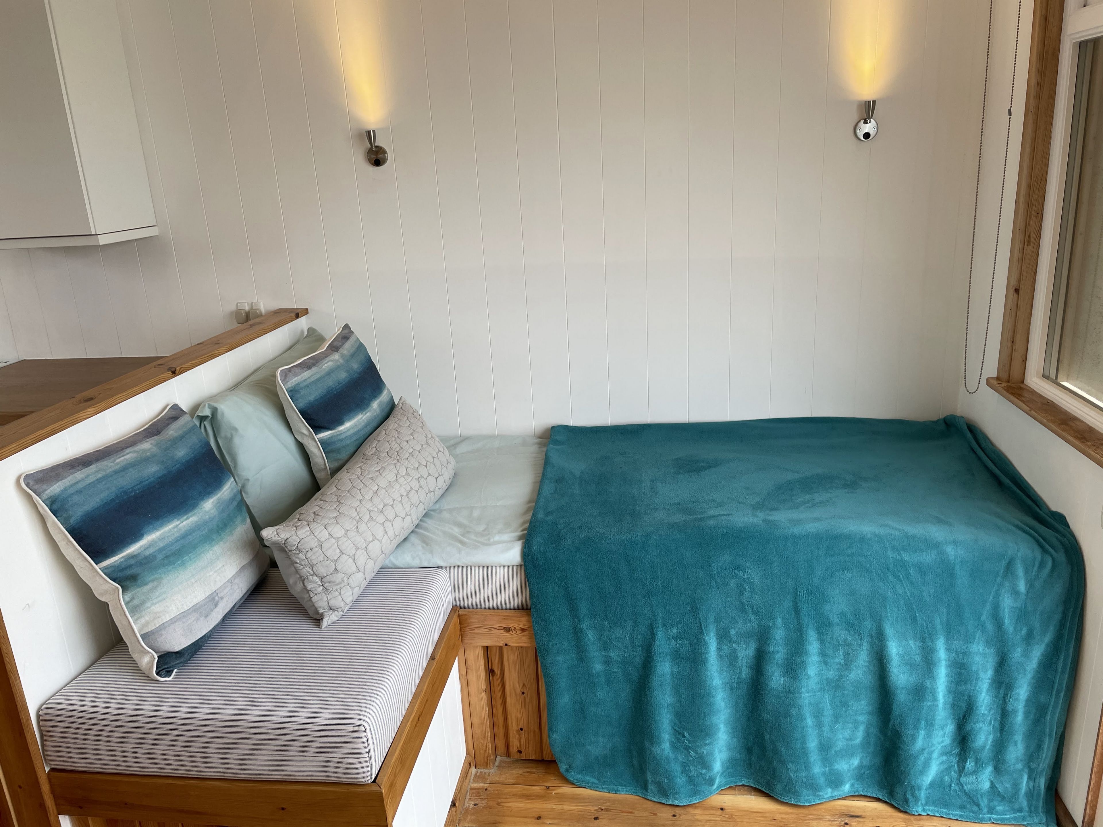 Un coin douillet aménagé pour se reposer, avec un banc, des coussins et une couverture de couleur turquoise.