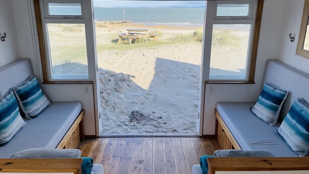 Habitación junto a la playa con dos zonas de descanso con cojines frente a un amplio ventanal.
