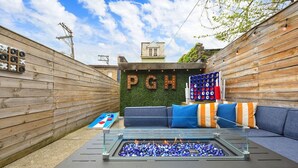 Un espace extérieur accueillant avec un foyer, une table de ping-pong et un mur orné des lettres « PGH ».