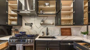 Une cuisine moderne avec des meubles de couleur sombre, une cuisinière à gaz, un four encastré et un dosseret en marbre.