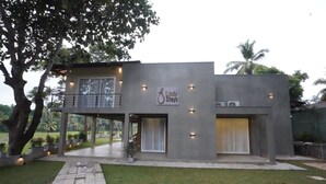 Un edificio moderno de dos pisos con un letrero que dice "Lindy Stays". Cuenta con un espacio exterior cubierto con balcón, un gran ventanal en la planta baja y un césped bien cuidado.