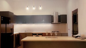 Una cocina moderna con gabinetes oscuros, una isla central y tres lámparas colgantes.