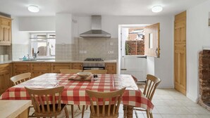 A kitchen with a checkered tablecloth, wooden chairs, a stove, and cabinets. - Historic Cottage & Garden nr Quantock Hills (Nether Stowey)