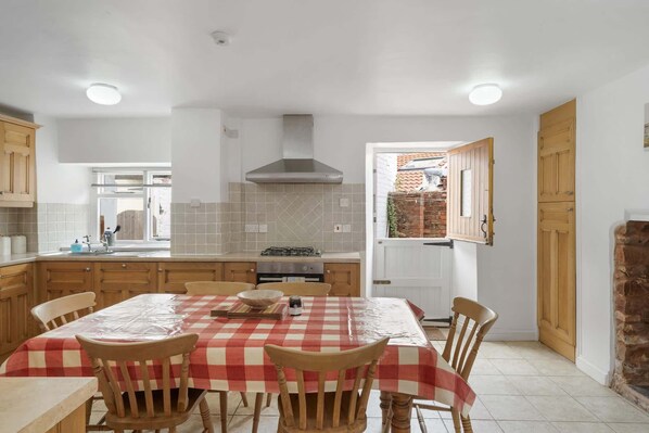 Une cuisine avec une nappe à carreaux, des chaises en bois, un poêle et des placards.