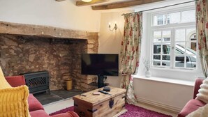 A cozy living room with a stone fireplace, a flat-screen TV, and a window with floral curtains.