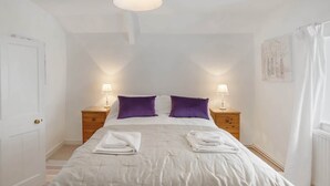 A bedroom with a bed, two nightstands, a hanging lamp, and a door. - Historic Cottage & Garden nr Quantock Hills (Nether Stowey)