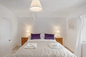 A bedroom with a bed, two nightstands, a hanging lamp, and a door. - Historic Cottage & Garden nr Quantock Hills (Nether Stowey)