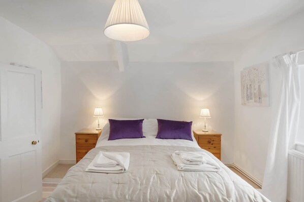 A bedroom with a bed, two nightstands, a hanging lamp, and a door. - Historic Cottage & Garden nr Quantock Hills (Nether Stowey)