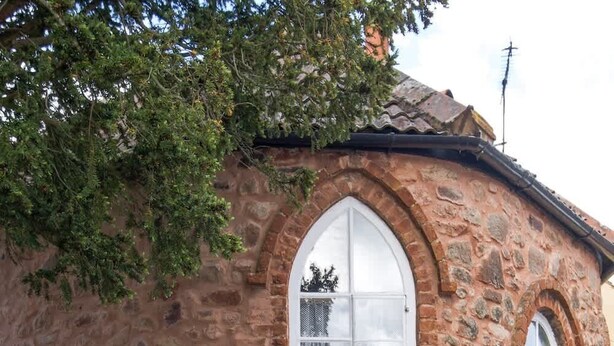 A stone building with arched windows and a door, a potted plant, and a sign that reads "The Cottage."