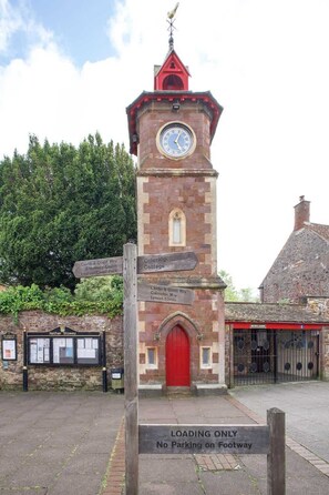 A clock tower with a red door and a sign indicating directions to nearby locations. - Historic Cottage & Garden nr Quantock Hills (Nether Stowey)