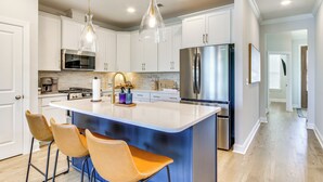Una cocina moderna con armarios blancos, electrodomésticos de acero inoxidable y una isla central con taburetes de bar.