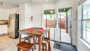 Eine Küche mit weißen Schränken, einem Edelstahlkühlschrank, einem Holztisch mit zwei roten Untersetzern und einem Deckenventilator.