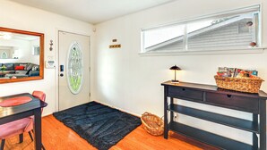 Ein Zimmer mit einem Esstisch, Stühlen, einem schwarzen Teppich, einem Korbwäscher, einer Lampe und einem Fenster mit Blick auf ein Haus.