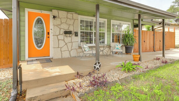 Ein Haus mit einer Stein-Fassade, einer orangefarbenen Tür und einer Veranda mit Gartenmöbeln.