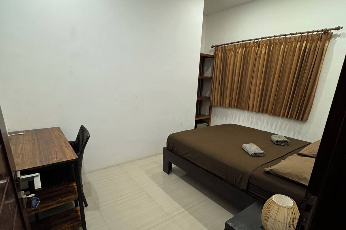 A bedroom with a bed, a desk, a chair, a lamp, and a window with curtains.