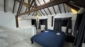 Une chambre dotée d’un grand lit, d’une baignoire intégrée et d’un plafond en pente avec des poutres en bois.