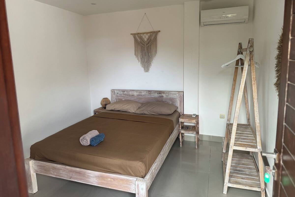 A bedroom with a wooden bed, a small bedside table, a hanging macrame wall decoration, and a wooden ladder.