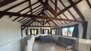 Une chambre spacieuse située sous les combles, avec un grand lit, un banc et une vue sur l’extérieur grâce à de grandes fenêtres.