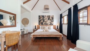 Ein geräumiges Schlafzimmer mit einem großen Bett, Holzboden, Deckenventilator und einem großen Fenster mit Vorhängen.