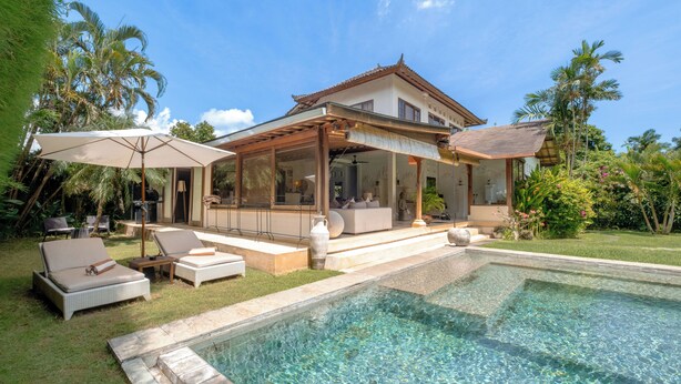 Ein modernes Haus mit Pool, Sitzgelegenheit im Freien und tropischer Bepflanzung.