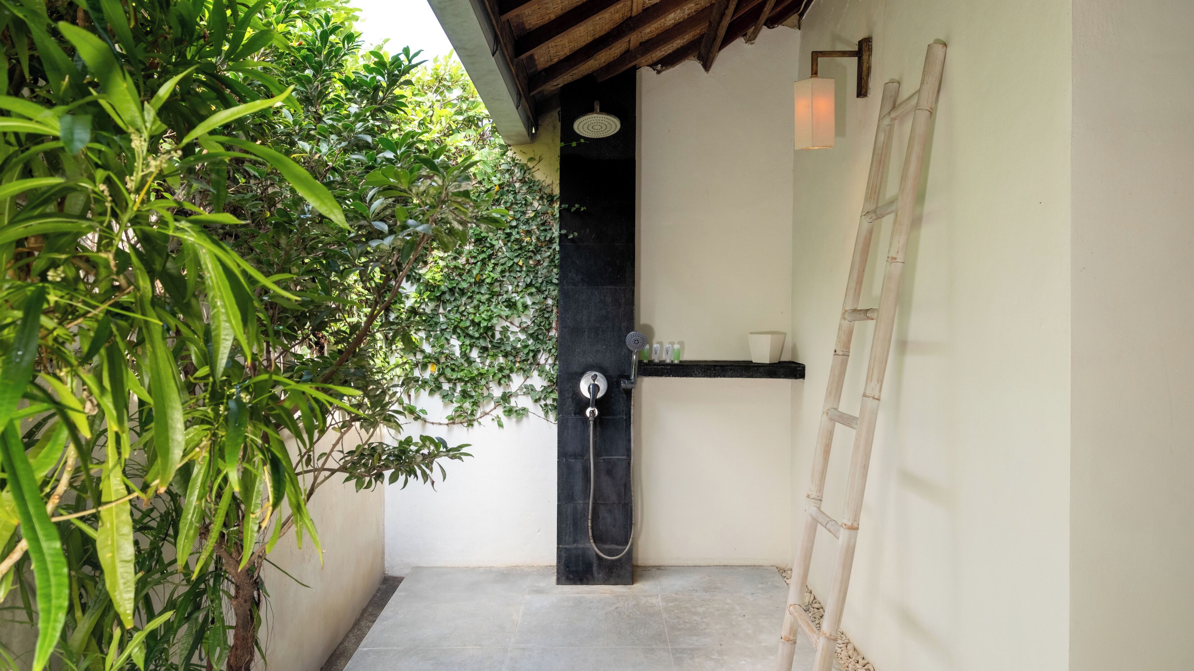 Zona de ducha con pared negra, escalera de madera y estante con artículos de aseo.