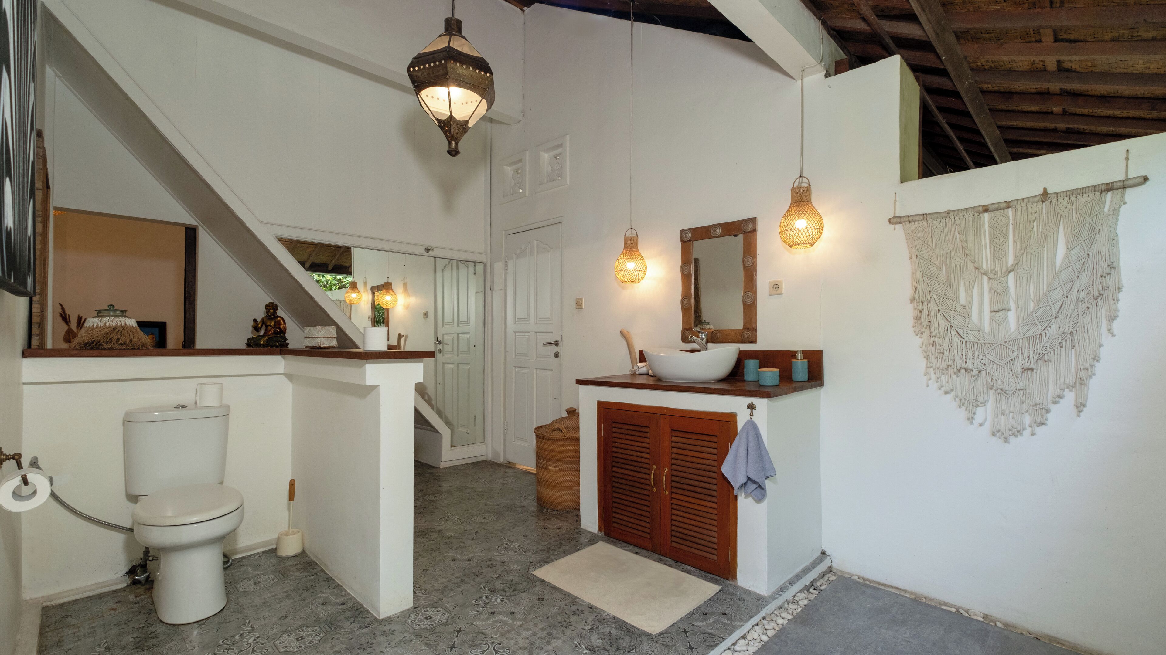 A bathroom with a toilet, sink, and shower area. There is a staircase leading to another room.