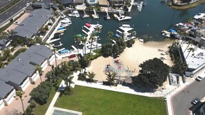 An aerial view of a marina with boats docked, a basketball court, and surrounding greenery.