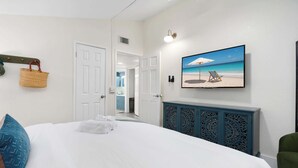 Une chambre d’hôtel avec un lit, un tableau représentant une scène de plage, une armoire bleue et une chaise verte.