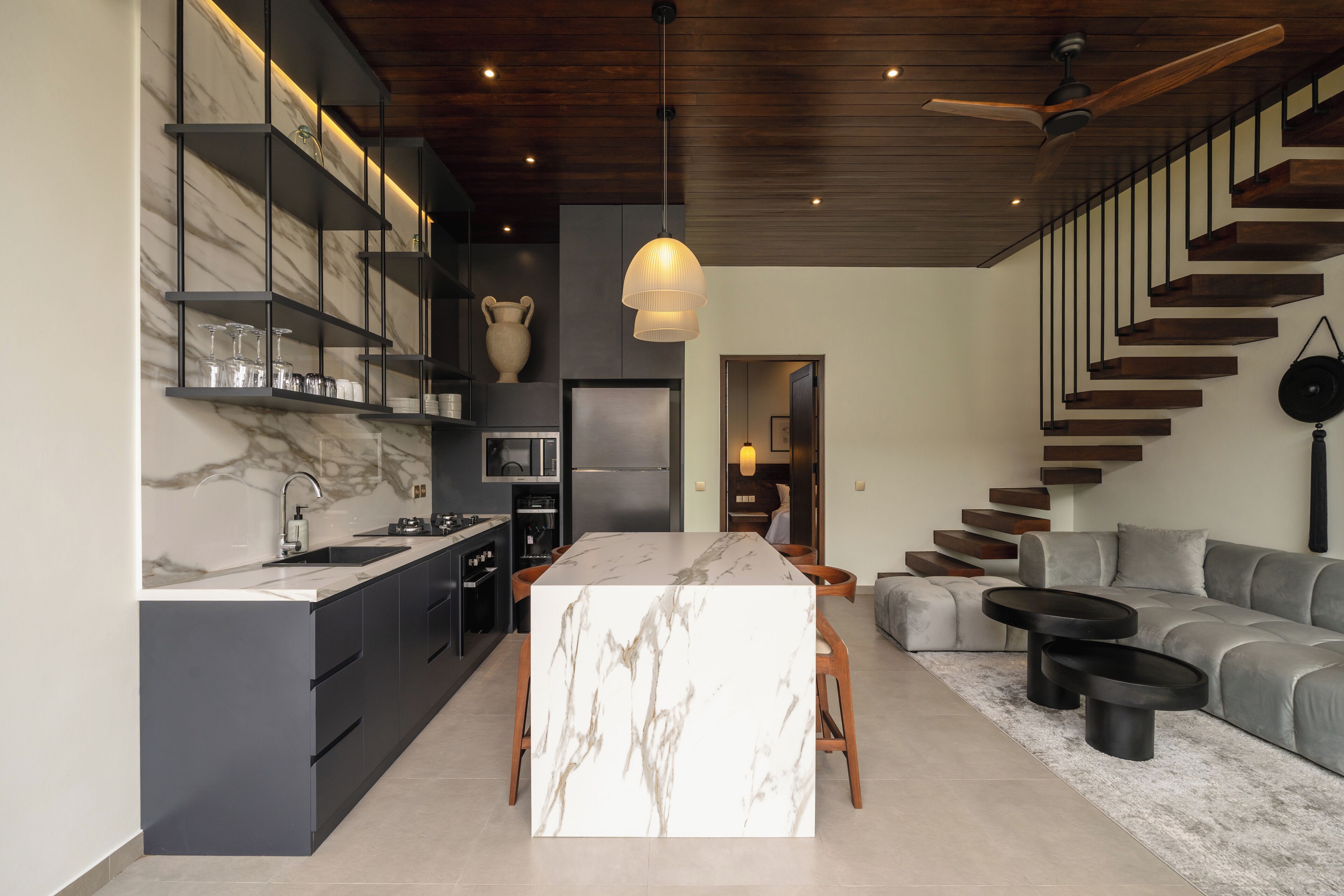 A modern kitchen with marble countertops, a central island, and built-in shelves.