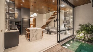 A modern kitchen with a marble island, wooden ceiling, and a glass-enclosed dining area. - Rocca Bella Loft 1 by Alfred in Bali (Canggu)