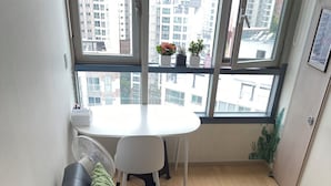 A modern living room with a black sofa, green cushions, a white table, and a large window offering a city view. - Seoul Apartment. Great location, close to tourist attractions, Wi-Fi. (Seoul)