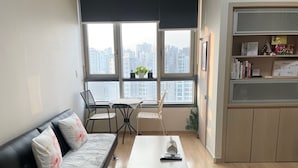 A modern living room with a black leather sofa, a wooden coffee table, and a dining area with a small table and chairs. Large windows provide a view of the cityscape. - Seoul Apartment. Great location, close to tourist attractions, Wi-Fi. (Seoul)