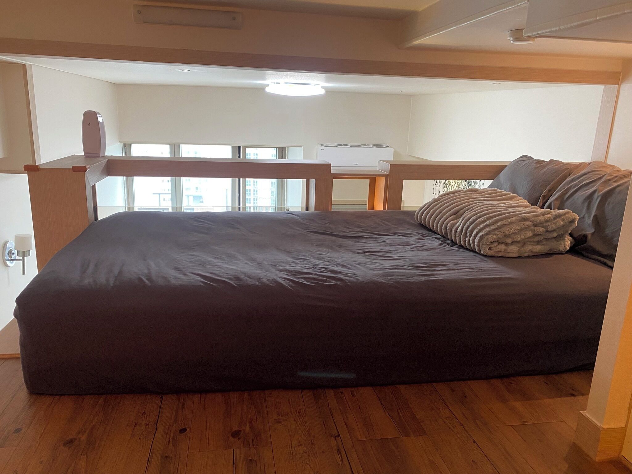 Un dormitorio con una cama grande, piso de madera y vistas a la ciudad a través de amplias ventanas.